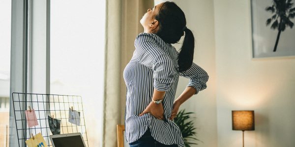 Rearview shot of a young woman suffering with back pain while working from home