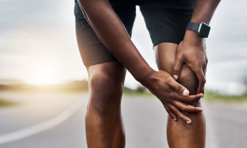 Closeup shot of a sporty man suffering with knee pain while exercising outdoors